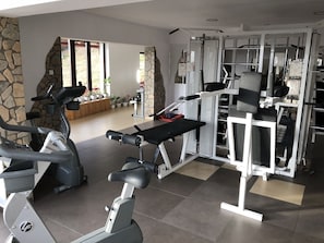 A gym with exercise equipment, a stone wall, and a view of the outdoors. - Complex Turistic Alpina Blazna (Sant)