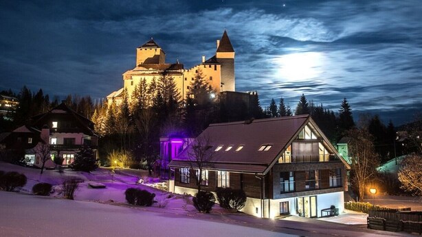 Un edificio parecido a un castillo con una torre, rodeado de árboles y nieve.