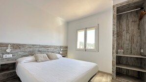 Un dormitori amb un llit gran, un capçal de fusta, una finestra amb vistes i un armari de fusta.