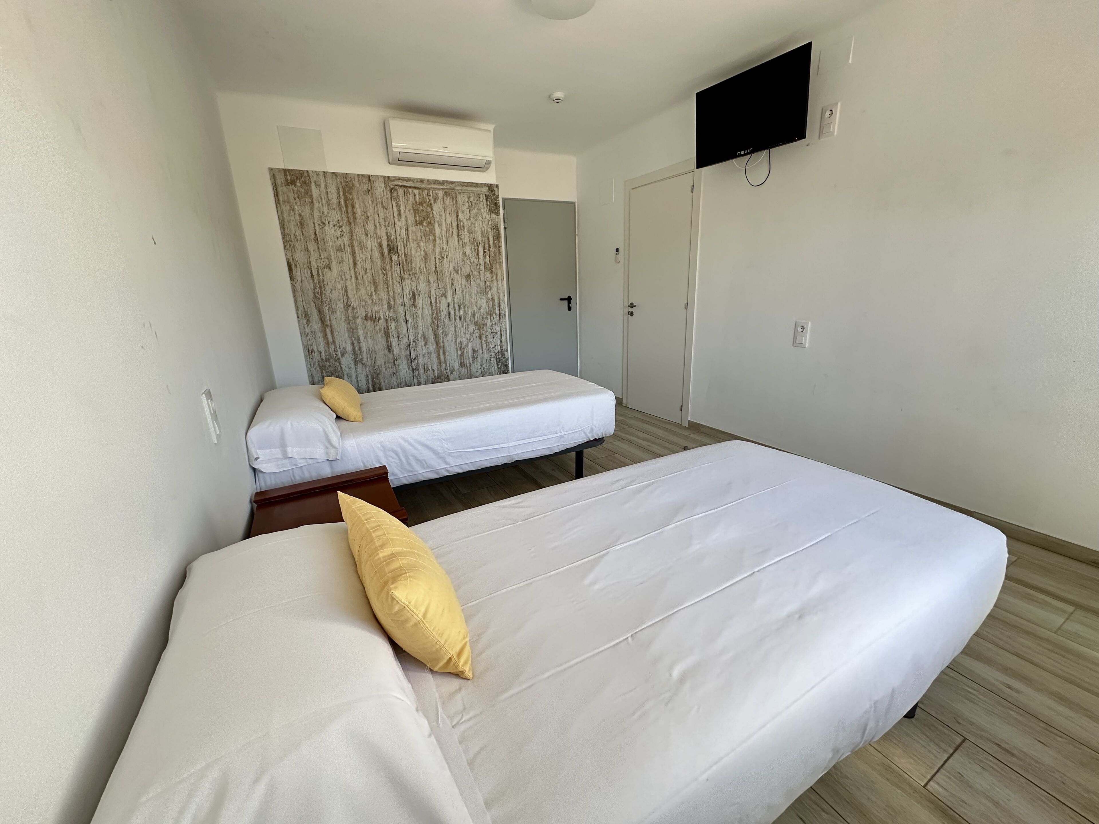 Una habitación de hotel con dos camas, un televisor montado en la pared y un aire acondicionado.