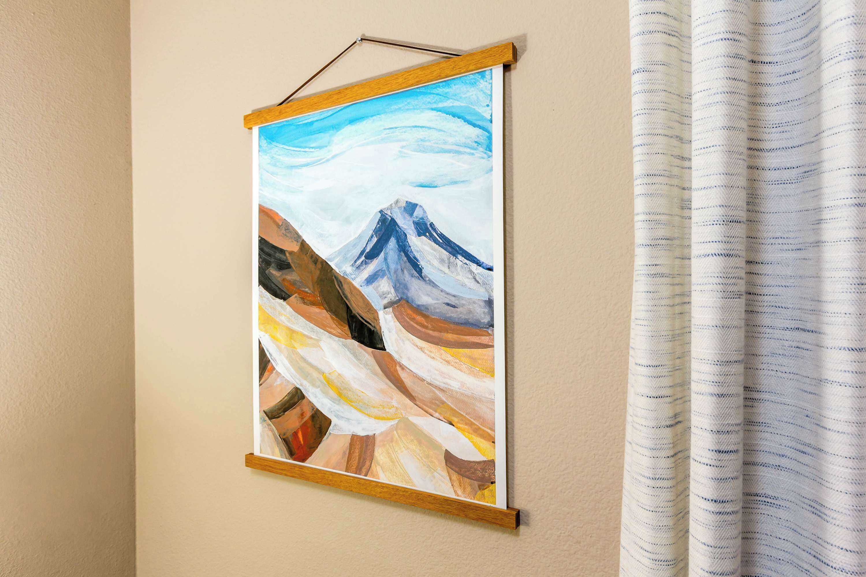 A framed painting of a mountain landscape on a wall.