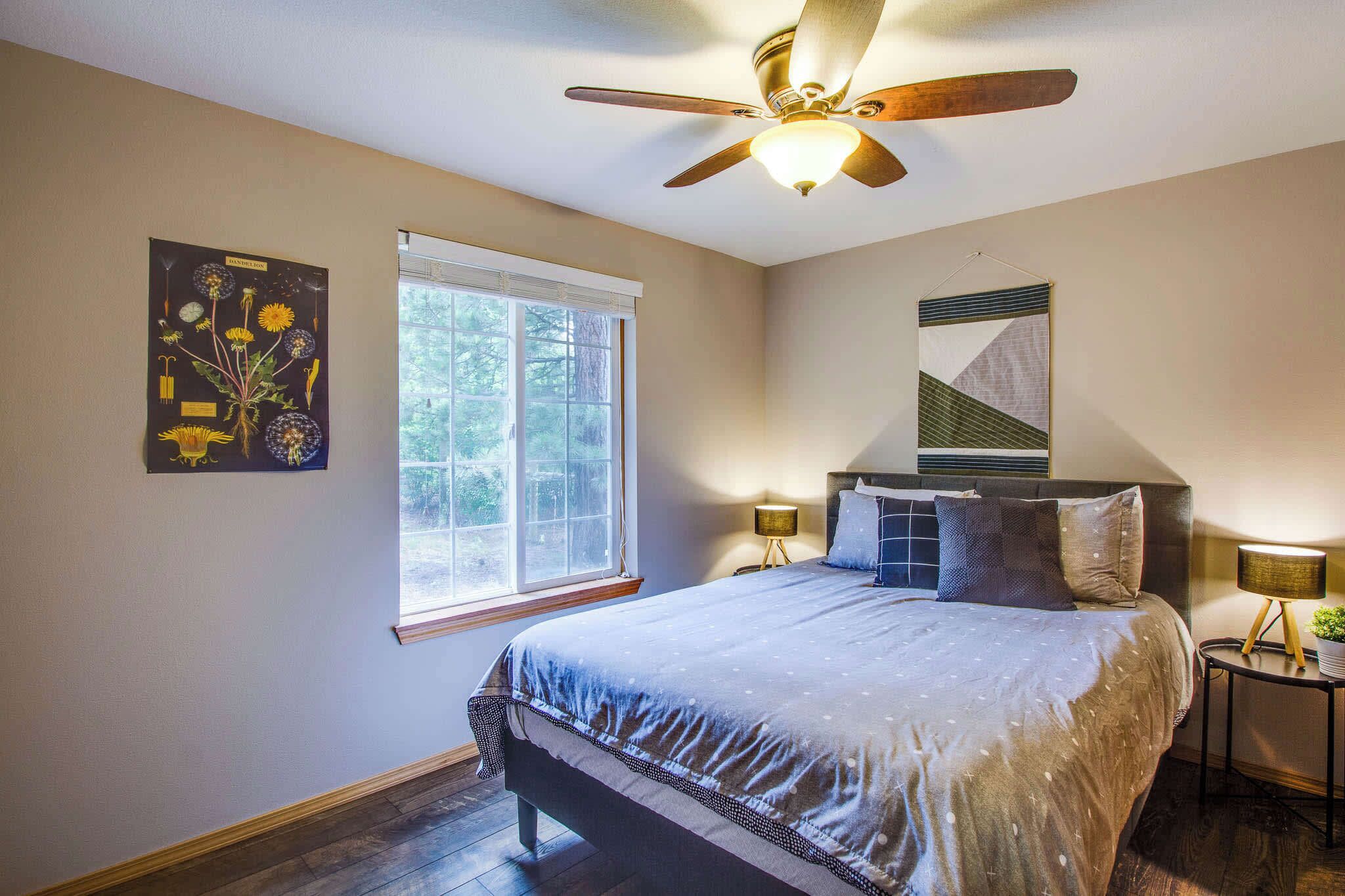 Une chambre à coucher comprenant un lit, un ventilateur de plafond, une fenêtre et une œuvre d’art accrochée au mur.
