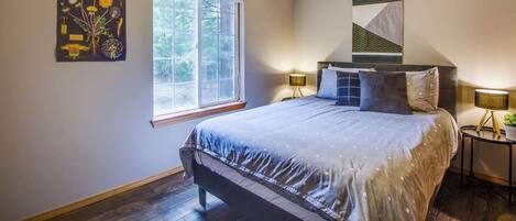 Une chambre à coucher comprenant un lit, un ventilateur de plafond, une fenêtre et une œuvre d’art accrochée au mur.