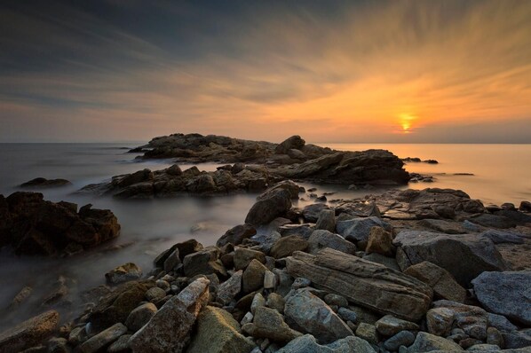 A rocky shoreline with a sunset in the background.