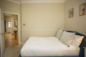 A bedroom with a large bed, a door leading to a hallway, and a radiator. - Quiet, City Garden Apt. Pets Allowed (PL) (Bath)