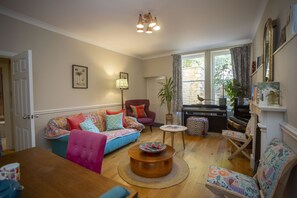 A cozy living room with a sofa, armchairs, a coffee table, and a piano. - Quiet, City Garden Apt. Pets Allowed (PL) (Bath)