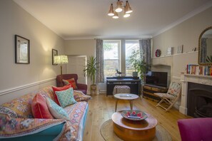 A living room with a sofa, armchair, coffee table, television, fireplace, and a bookshelf. - Quiet, City Garden Apt. Pets Allowed (PL) (Bath)