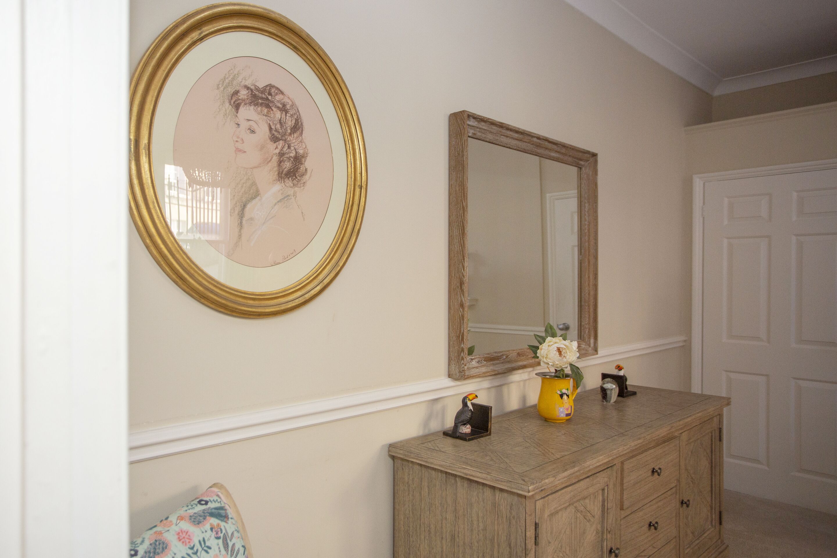 Une pièce comprenant une commode en bois, un miroir et un portrait encadré accroché au mur.