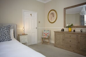 A bedroom with a bed, a nightstand, a chair, a dresser, and a mirror.