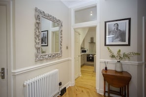 A hallway with a white radiator, a mirror, a framed photograph, and a wooden table with a vase of flowers. - Quiet, City Garden Apt. Pets Allowed (PL) (Bath)