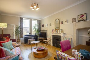 A cozy living room with a sofa, chairs, a coffee table, a fireplace, and a television. - Quiet, City Garden Apt. Pets Allowed (PL) (Bath)