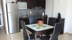 A compact kitchen with dark cabinets, a stainless steel refrigerator, a microwave, and a coffee machine. There is a glass-top dining table with four chairs. - Residencial complex les marines  (Roses)