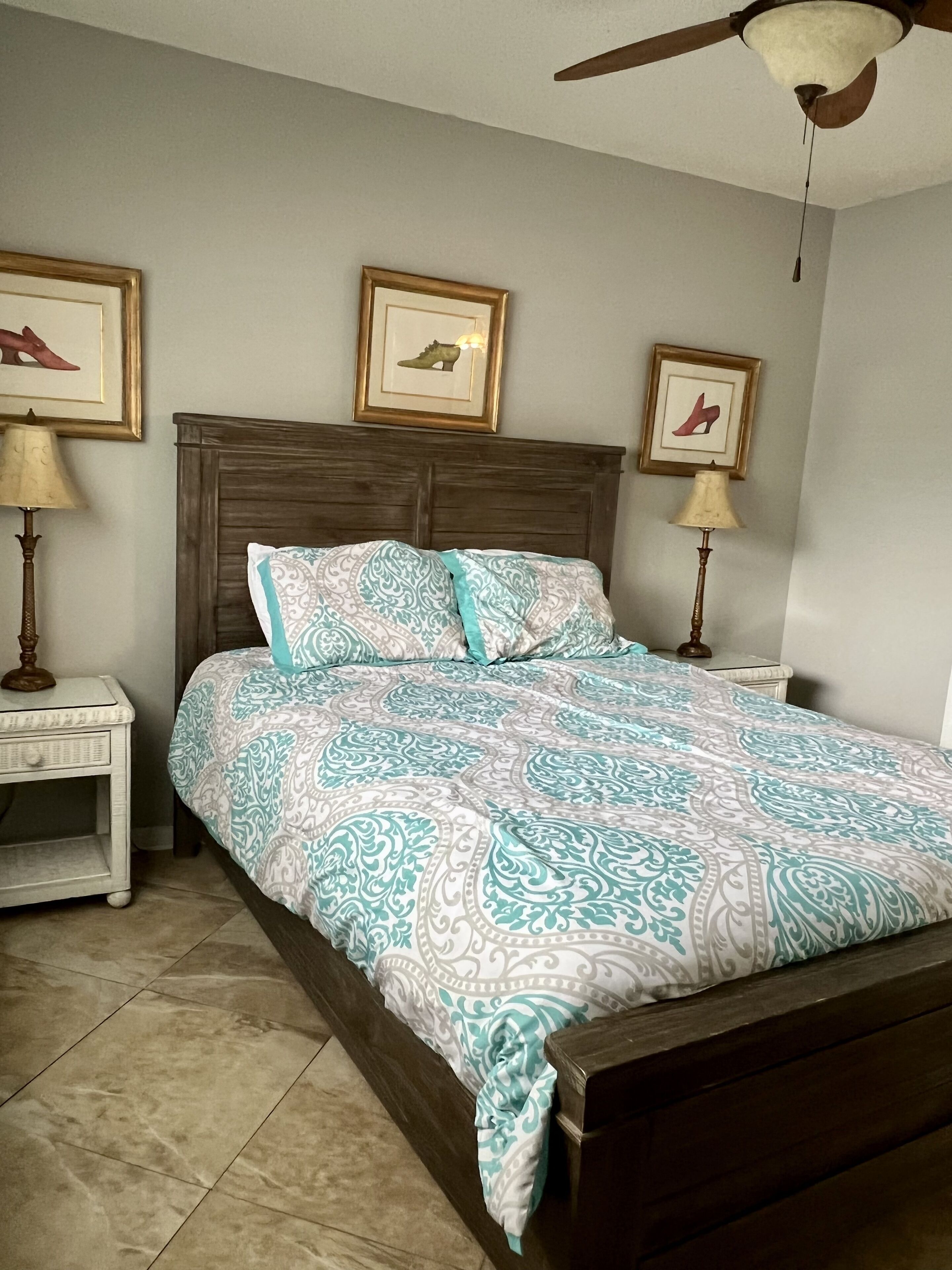A bedroom with a wooden bed, patterned bedding, two bedside tables with lamps, and framed pictures on the wall.