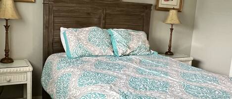 A bedroom with a wooden bed, patterned bedding, two bedside tables with lamps, and framed pictures on the wall.