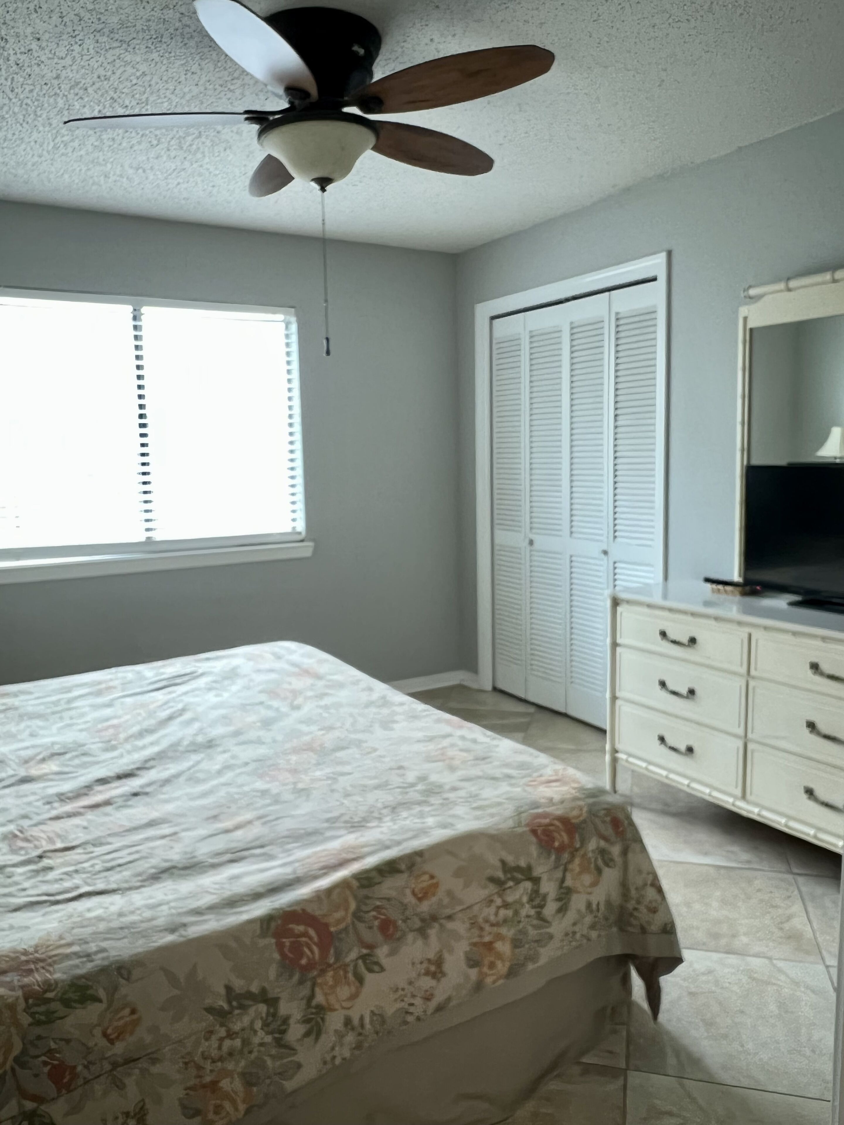 Ein Schlafzimmer mit Bett, Deckenventilator, Kleiderschrank und Fenster.