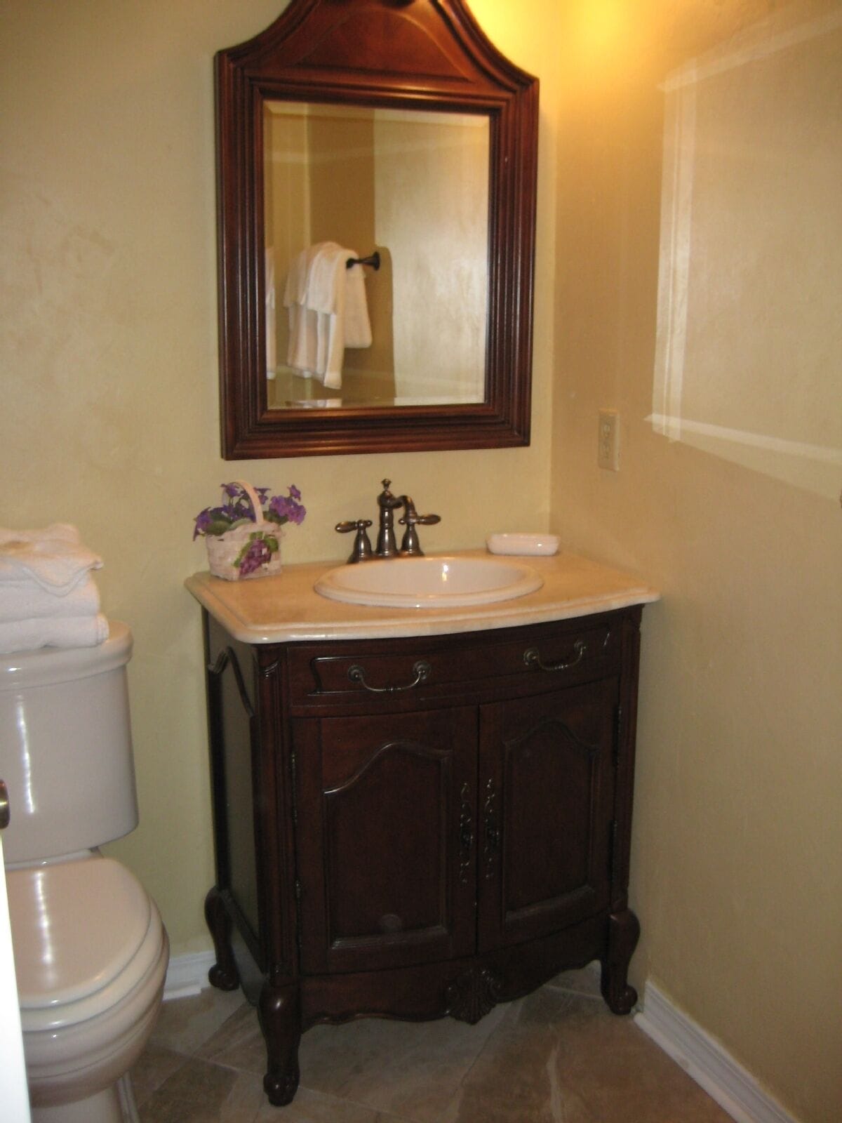 A bathroom with a wooden vanity, a white sink, and a mirror above the sink.