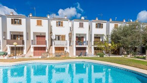 A row of white buildings with balconies, a swimming pool, and a clear blue sky.