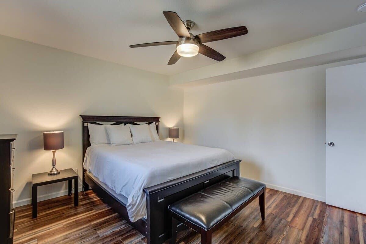 Une chambre à coucher avec un lit, des lampes de chevet, un banc, un ventilateur de plafond et une porte.