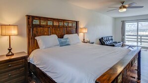 Un dormitorio con una cama grande, cabecera de madera, dos lámparas de noche, un sillón de cuero negro y un ventilador de techo.