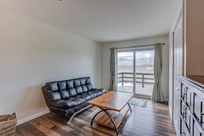 Una habitación con un sofá de cuero negro, una mesa de centro de madera y vistas a un paisaje nevado a través de un amplio ventanal con cortinas.