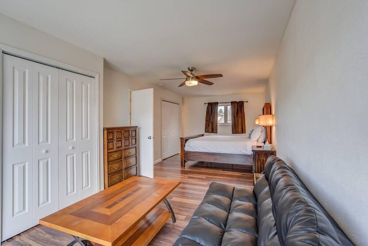 A compact room with a bed, a wooden table, a leather sofa, and a ceiling fan.