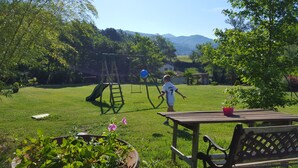 A grassy backyard with a swing set, a slide, and a table with a bench. - cottage with a view of the river (Le Tech)