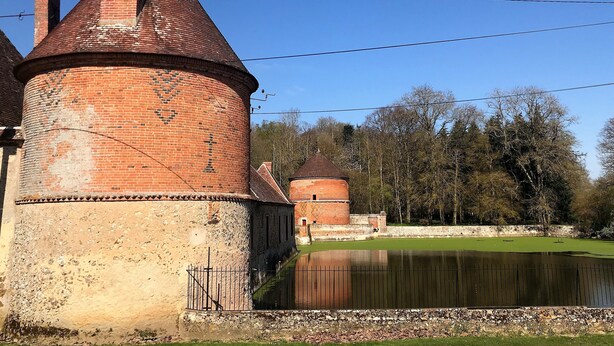 Ein historischer Backsteinturm mit einer kegelförmigen Haube, einem kreisförmigen Wasserspiel und einer Steinmauer.