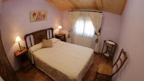 Une chambre à coucher avec un lit, deux tables de chevet avec des lampes, une chaise et une fenêtre avec des rideaux.