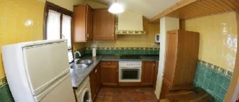 A compact kitchen with basic appliances, a washing machine, and a small dining area with a wooden table and chairs.