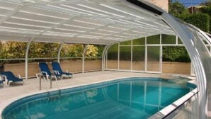 Une piscine intérieure dotée d’un espace couvert, de chaises longues bleues et offrant une vue dégagée sur la végétation environnante.