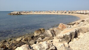 Uma praia rochosa com água cristalina, faixa de areia e guarda-sóis de praia.