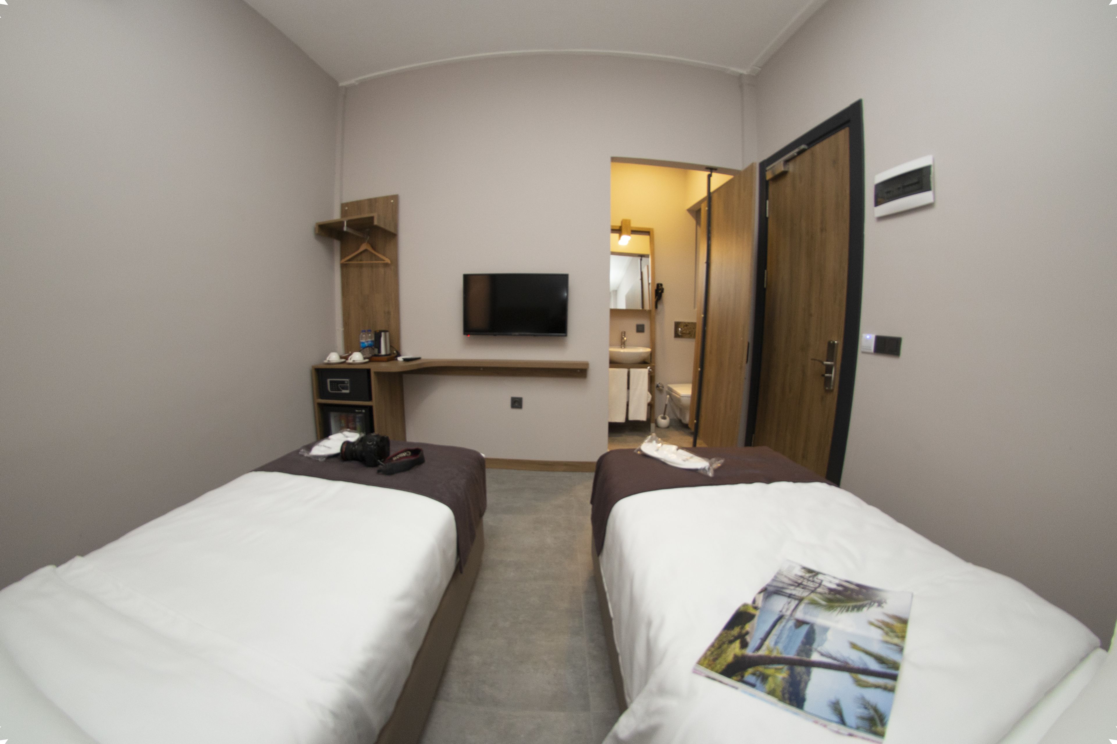 A hotel room with two single beds, a flat-screen TV mounted on the wall, a small desk with a chair, and a wooden wardrobe.