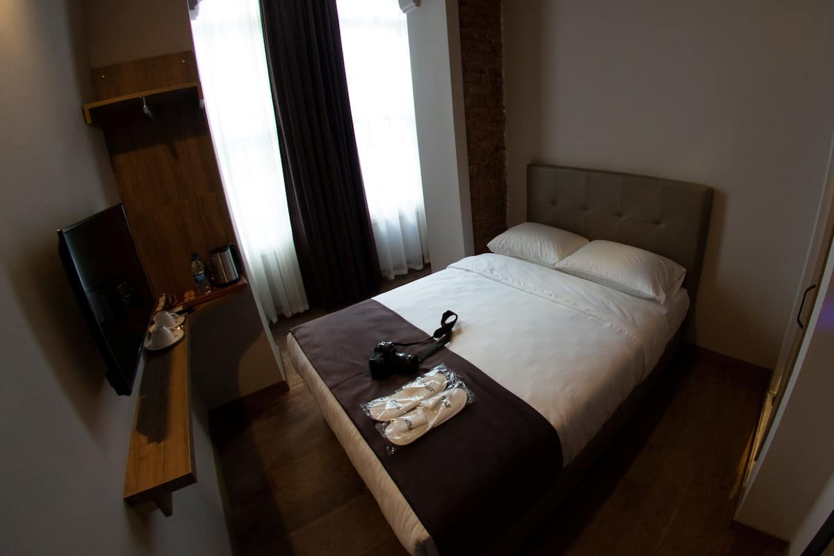 A hotel room with a bed, a TV, a desk, and a window with curtains.