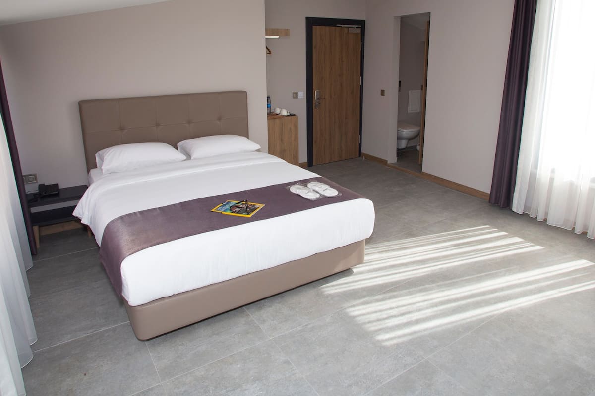 A hotel room with a large bed, a bedside table, a wardrobe, and a bathroom visible through an open door.