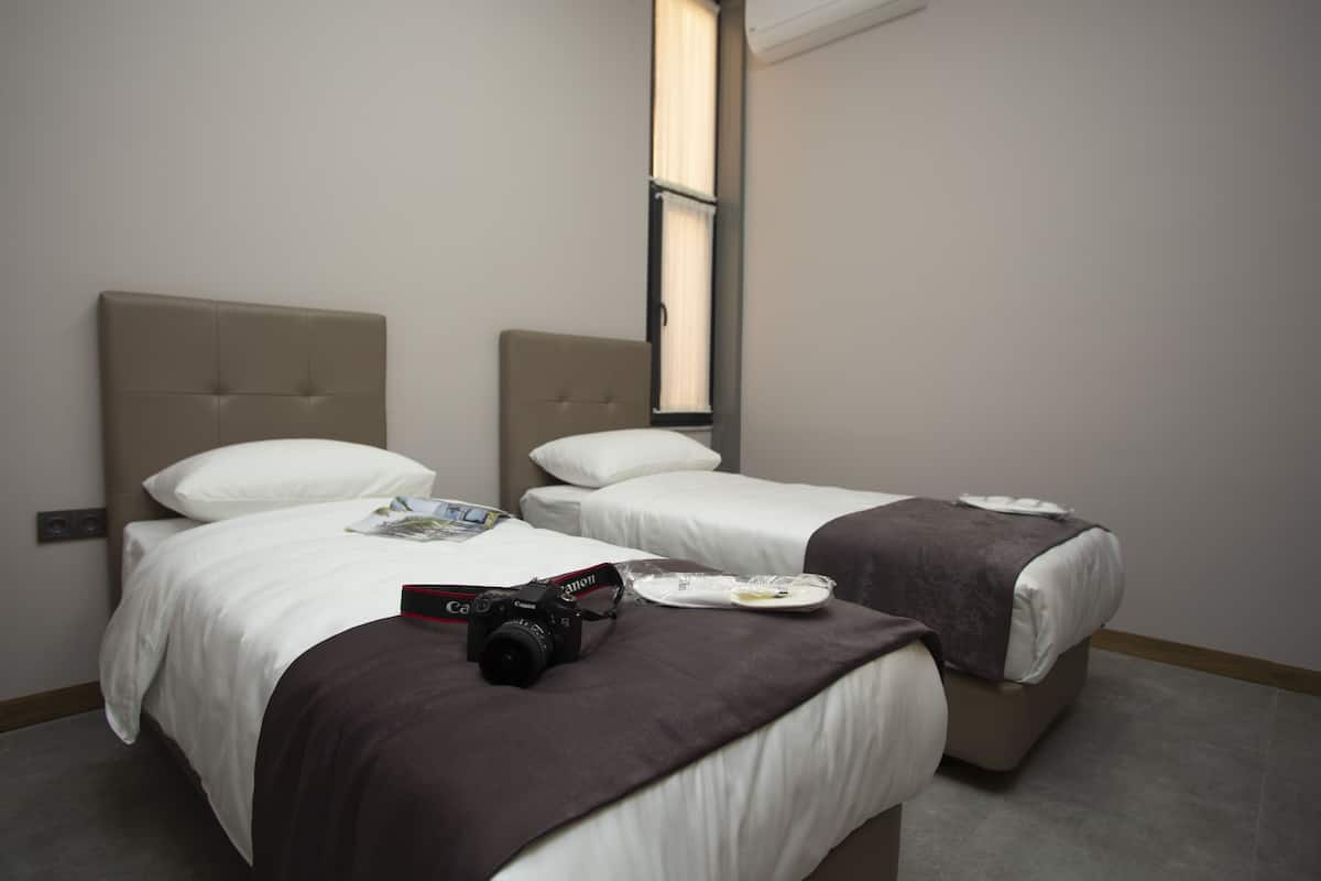 A hotel room with two beds, a window, and a camera on the bed.