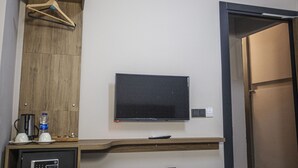 A hotel room with a mounted flat-screen TV, a wooden cabinet with a hanging coat rack, a small table with a coffee maker and cups, and a door leading to another room. - Jurnal Hotel (Istanbul)