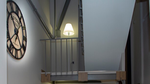 A modern interior with a wooden staircase, a wall-mounted clock, and a desk area with a lamp. - Jurnal Hotel (Istanbul)