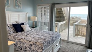 A bedroom with a bed, a nightstand, a lamp, and a view of the beach through a sliding glass door. - OCEANFRONT ! Family fun steps from the beach! Pet friendly, linens included! (North Topsail Beach)