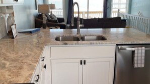 A kitchen with white cabinets, a stainless steel refrigerator, a double sink, and a ceiling fan. - OCEANFRONT ! Family fun steps from the beach! Pet friendly, linens included! (North Topsail Beach)