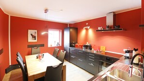 Una cocina moderna con paredes rojas, una mesa de comedor con sillas y un horno empotrado.