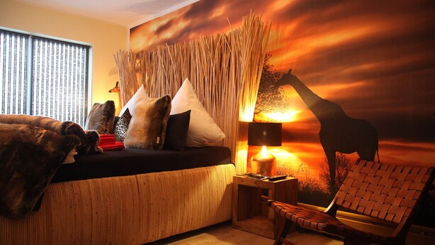 Una habitación acogedora con sofá, almohadas, una lámpara y un mural de jirafa en la pared.
