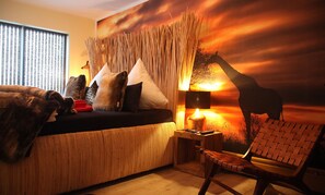 Una habitación acogedora con sofá, almohadas, una lámpara y un mural de jirafa en la pared.