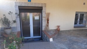 Une entrée d’immeuble avec une porte en verre, des plantes en pot et un panneau d’accueil.