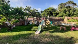 Un jardin avec une pelouse verdoyante, un arbre, une balançoire et une clôture en bois.