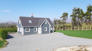 Een twee verdiepingen tellend huis met een grijs dak, witte details en een oprit met grind.