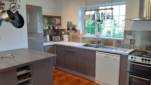 Een moderne keuken met grijze kastjes, een houten visgraatvloer, een inbouwvaatwasser, een fornuis en een raam met uitzicht op groen.