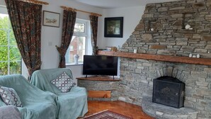 Een gezellige woonkamer met een stenen openhaard, een televisie en een comfortabele zithoek.