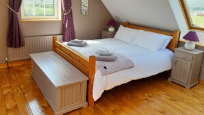 Een slaapkamer met een houten bed, een nachtkastje, gordijnen voor het raam en uitzicht op de omgeving.