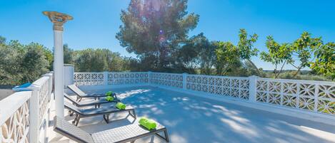 Een zonnig terras met lounge fauteuils en een pergola.