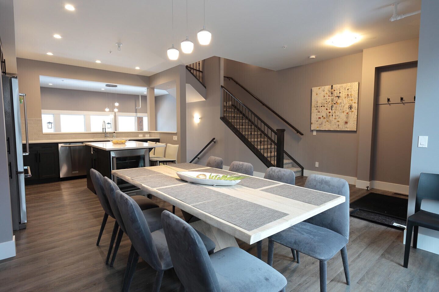 Une cuisine moderne dotée d’un îlot central, un coin repas avec une longue table et des chaises, et un escalier menant à un niveau supérieur.